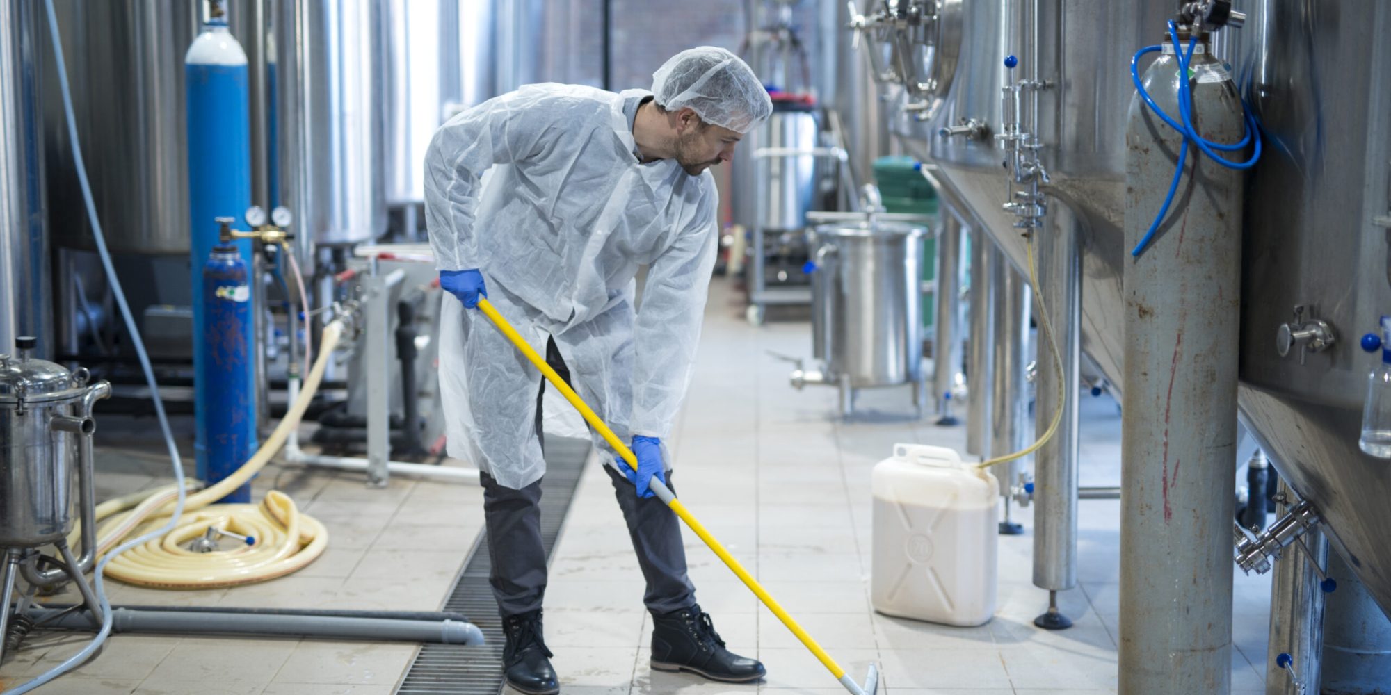 Professional industrial cleaner in protective uniform cleaning floor of food processing plant. Cleaning services.